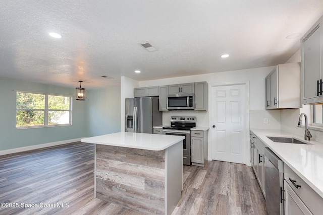 kitchen with sink, gray cabinets, appliances with stainless steel finishes, hanging light fixtures, and a kitchen island