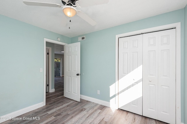 unfurnished bedroom with a textured ceiling, light hardwood / wood-style flooring, a closet, and ceiling fan