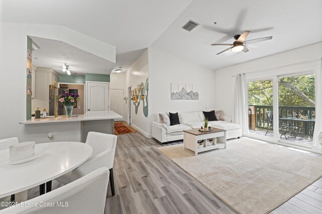 living room with vaulted ceiling, ceiling fan, and light wood-type flooring