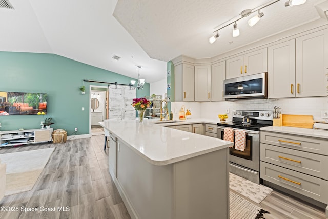 kitchen with sink, gray cabinetry, kitchen peninsula, stainless steel appliances, and a barn door