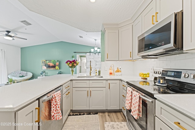 kitchen featuring sink, vaulted ceiling, appliances with stainless steel finishes, kitchen peninsula, and light hardwood / wood-style floors