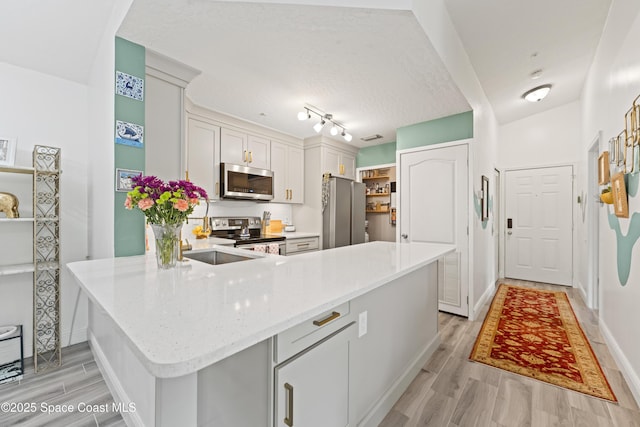 kitchen with light hardwood / wood-style floors, stainless steel appliances, kitchen peninsula, and light stone countertops