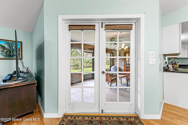 entryway featuring vaulted ceiling, sink, light hardwood / wood-style floors, a textured ceiling, and french doors