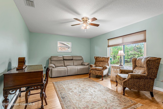 living room with ceiling fan, light hardwood / wood-style floors, and a textured ceiling