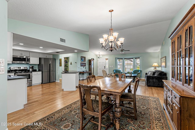 dining room featuring ceiling fan with notable chandelier, a raised ceiling, vaulted ceiling, and light hardwood / wood-style flooring