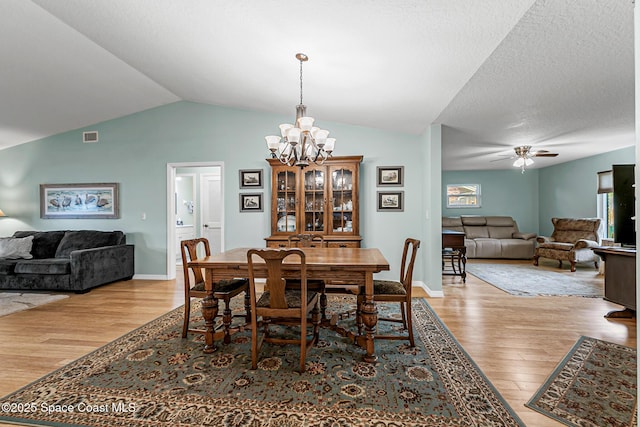 dining room featuring lofted ceiling, ceiling fan with notable chandelier, light hardwood / wood-style flooring, and a textured ceiling