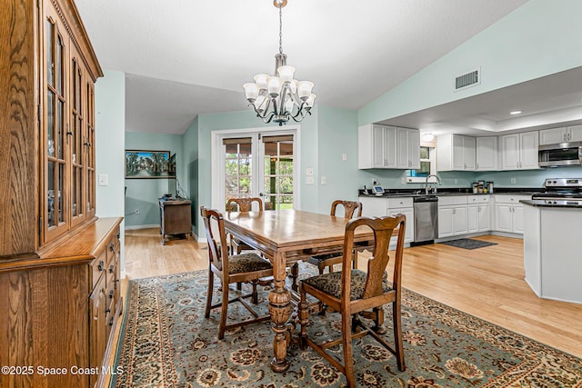 dining area with lofted ceiling, sink, light hardwood / wood-style floors, french doors, and a chandelier