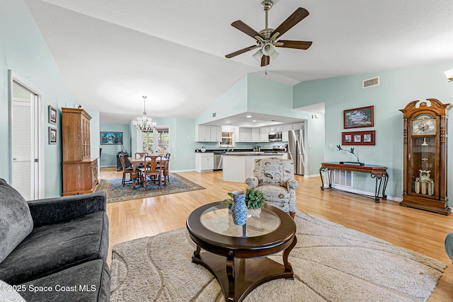 living room with ceiling fan with notable chandelier, lofted ceiling, and light hardwood / wood-style floors