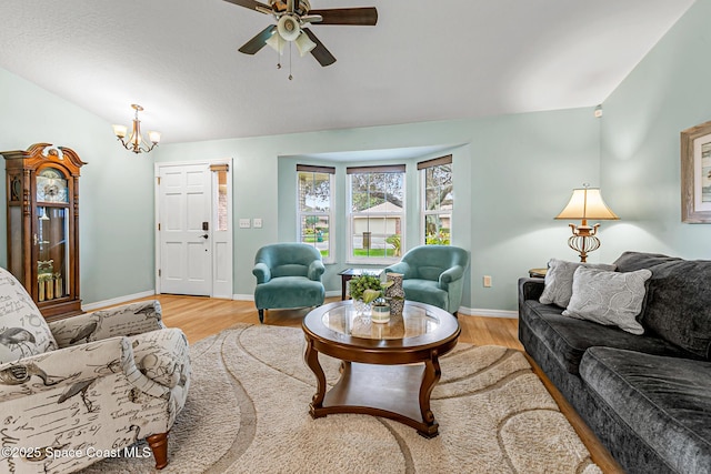 living room with light hardwood / wood-style flooring, ceiling fan with notable chandelier, and vaulted ceiling