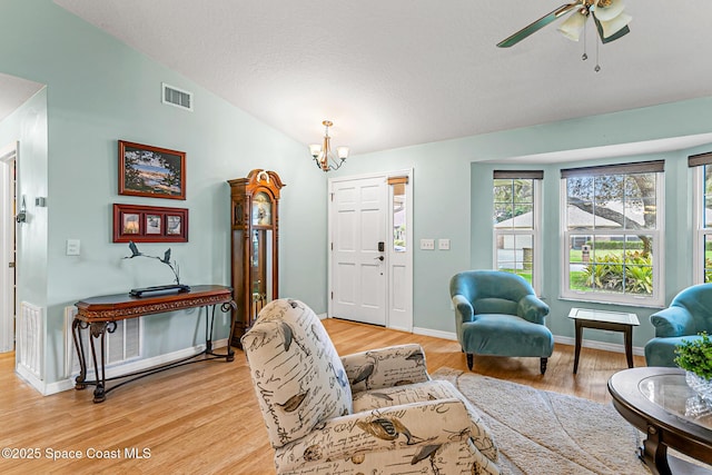 living room with ceiling fan with notable chandelier, lofted ceiling, and light hardwood / wood-style floors