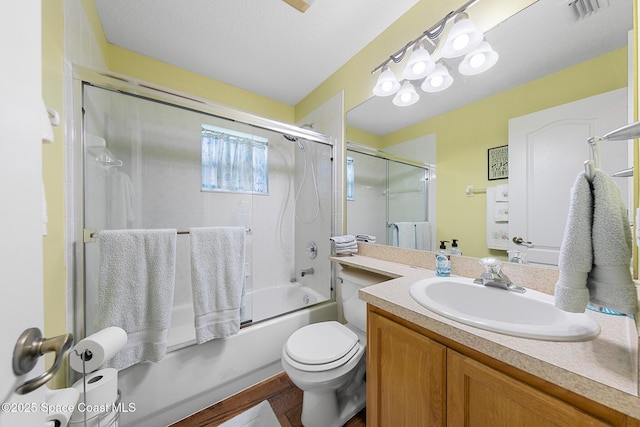 full bathroom with bath / shower combo with glass door, vanity, toilet, and a textured ceiling