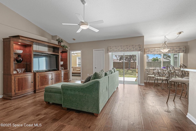 living room featuring dark hardwood / wood-style flooring, a textured ceiling, vaulted ceiling, and ceiling fan