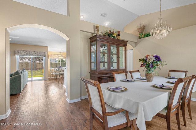 dining area featuring an inviting chandelier, vaulted ceiling, and wood-type flooring