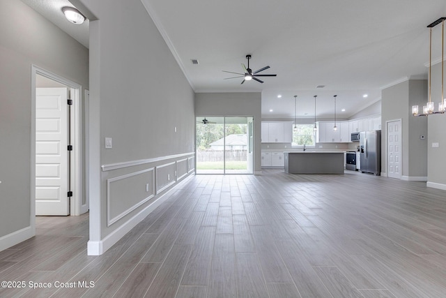 unfurnished living room featuring crown molding, ceiling fan with notable chandelier, light hardwood / wood-style flooring, and lofted ceiling