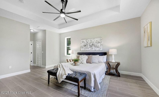 bedroom with a tray ceiling, wood finish floors, a ceiling fan, and baseboards