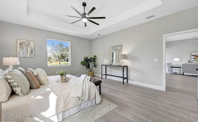 bedroom featuring visible vents, baseboards, ceiling fan, a tray ceiling, and wood finish floors