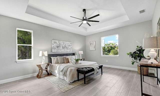 bedroom with light wood-style floors, a raised ceiling, visible vents, and baseboards