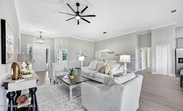 living room featuring ceiling fan with notable chandelier, ornamental molding, wood finished floors, and visible vents