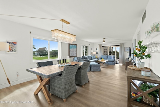 dining area featuring ceiling fan with notable chandelier, a wealth of natural light, and light hardwood / wood-style floors