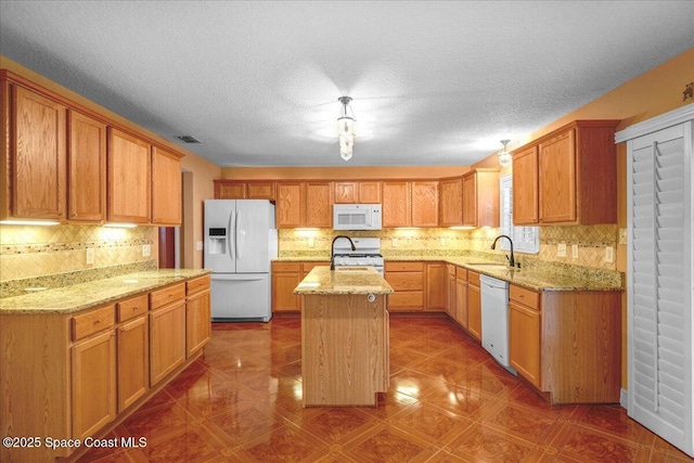 kitchen featuring light stone countertops, a kitchen island with sink, sink, and white appliances