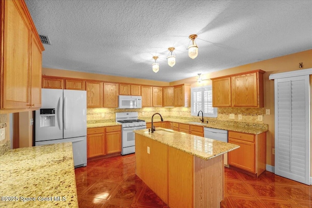 kitchen featuring light stone counters, white appliances, sink, and a center island with sink