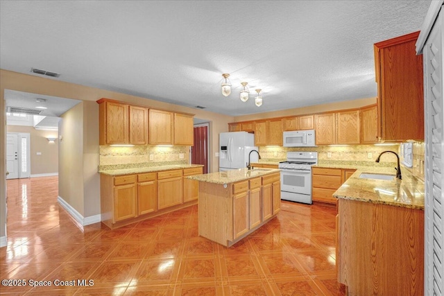 kitchen featuring sink, white appliances, light stone counters, a center island with sink, and decorative backsplash