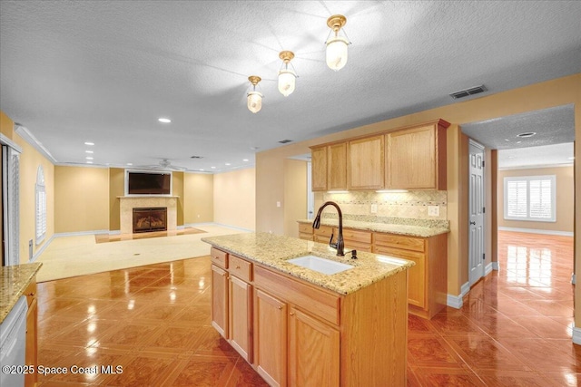 kitchen with sink, a kitchen island with sink, white dishwasher, light stone countertops, and decorative backsplash