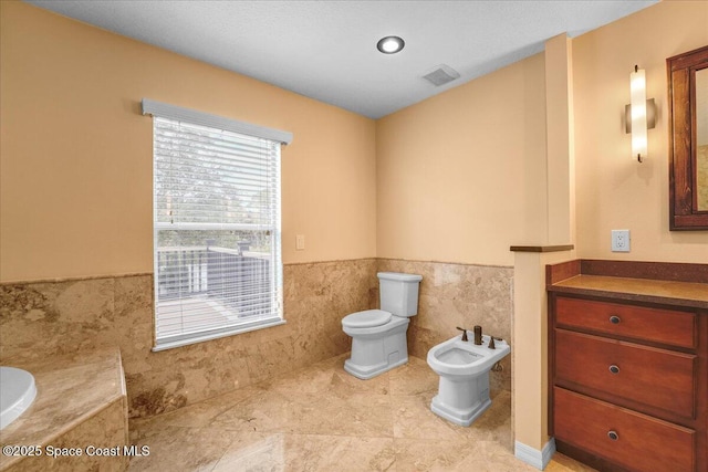 bathroom featuring toilet, tile walls, a bidet, a bathing tub, and tile patterned flooring