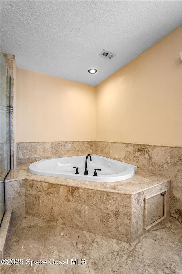 bathroom featuring tiled bath and a textured ceiling