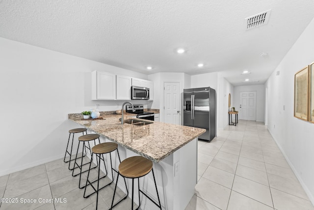 kitchen featuring visible vents, light stone counters, a peninsula, stainless steel appliances, and a sink