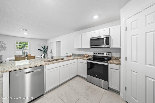 kitchen with light tile patterned floors, stainless steel appliances, a peninsula, a sink, and light stone countertops