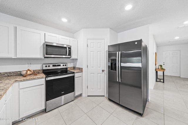 kitchen with light tile patterned floors, a textured ceiling, light stone counters, white cabinetry, and appliances with stainless steel finishes