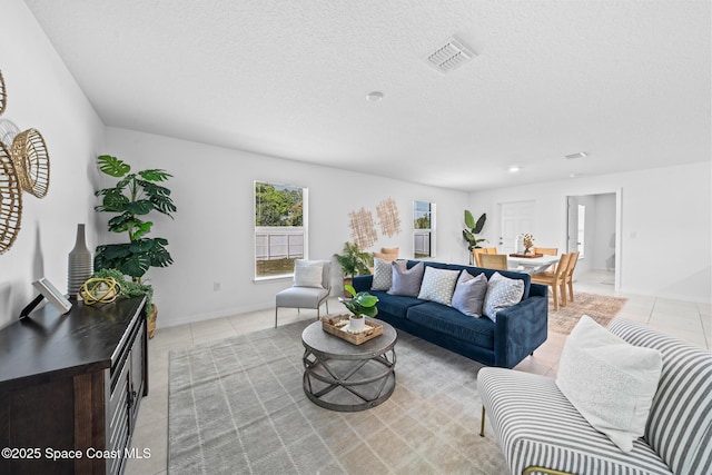 living room featuring light tile patterned floors, a textured ceiling, visible vents, and baseboards