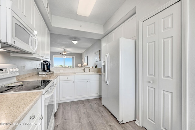 kitchen with light countertops, light wood-style flooring, white cabinets, a sink, and white appliances