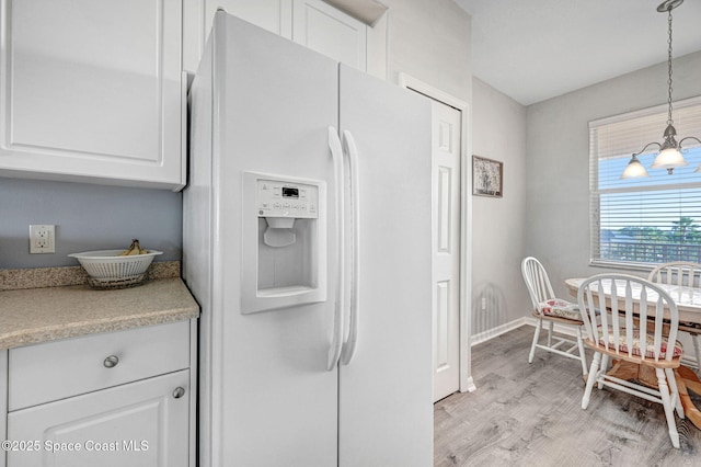 kitchen featuring white refrigerator with ice dispenser, light countertops, decorative light fixtures, and white cabinets