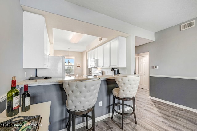 kitchen featuring visible vents, a breakfast bar area, a peninsula, light countertops, and white cabinetry