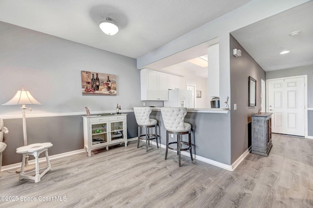 kitchen featuring a breakfast bar area, a peninsula, light countertops, white fridge with ice dispenser, and white cabinetry