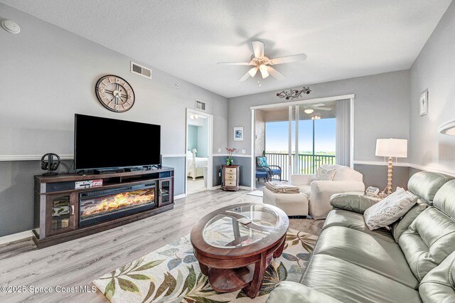 living room with light wood-type flooring, a textured ceiling, visible vents, and a ceiling fan