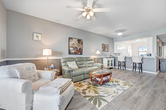 living room with ceiling fan, baseboards, and light wood-style floors