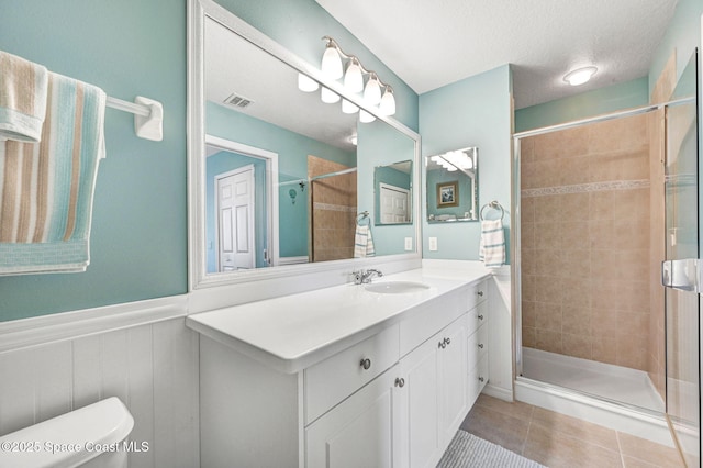 bathroom with a stall shower, a wainscoted wall, tile patterned flooring, a textured ceiling, and vanity