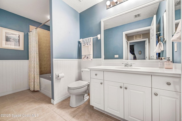 full bathroom featuring toilet, tile patterned flooring, visible vents, and wainscoting