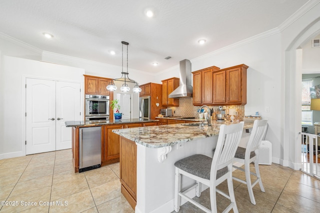 kitchen with brown cabinetry, pendant lighting, a peninsula, and wall chimney exhaust hood