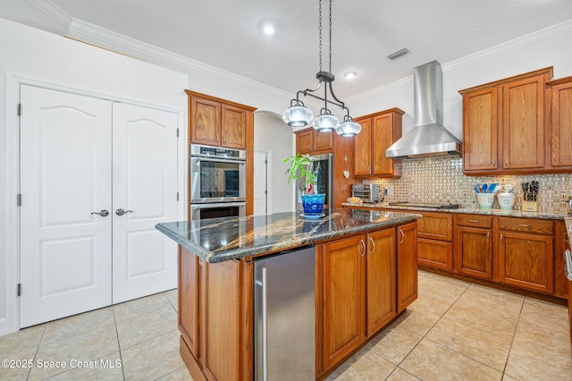 kitchen with double oven, visible vents, hanging light fixtures, wall chimney range hood, and a center island