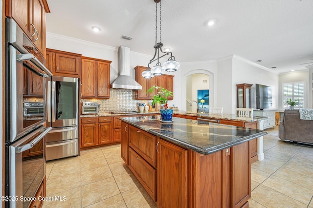 kitchen with a kitchen island, open floor plan, hanging light fixtures, wall chimney range hood, and freestanding refrigerator