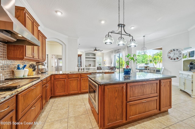 kitchen with ornamental molding, pendant lighting, wall chimney range hood, and light tile patterned floors