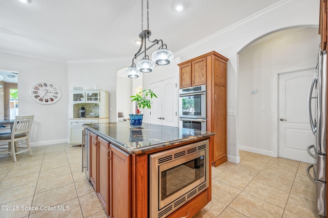 kitchen featuring arched walkways, stainless steel appliances, a center island, hanging light fixtures, and brown cabinets