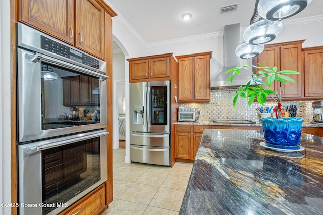 kitchen with light tile patterned floors, dark stone counters, wall chimney exhaust hood, stainless steel appliances, and crown molding