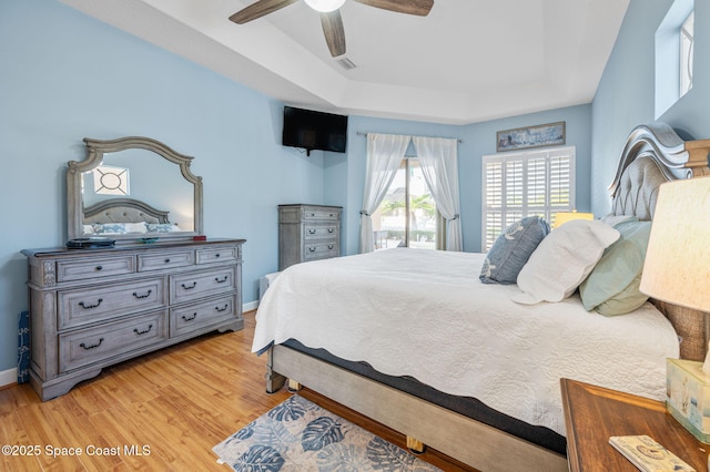 bedroom with a ceiling fan, light wood-style flooring, a tray ceiling, and baseboards