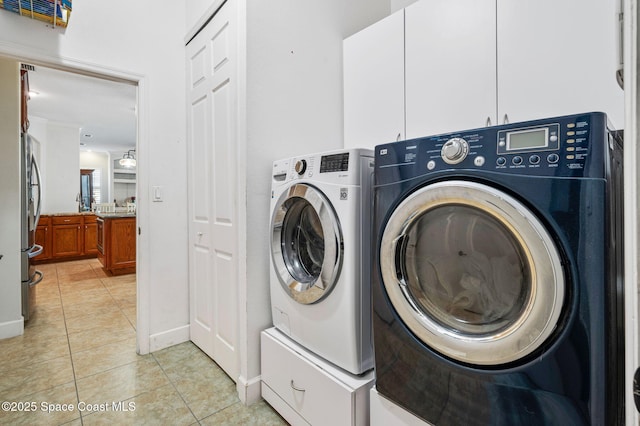 laundry room featuring washing machine and dryer, cabinet space, baseboards, and light tile patterned floors