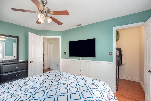 bedroom featuring wood-type flooring, a spacious closet, ceiling fan, a textured ceiling, and a closet